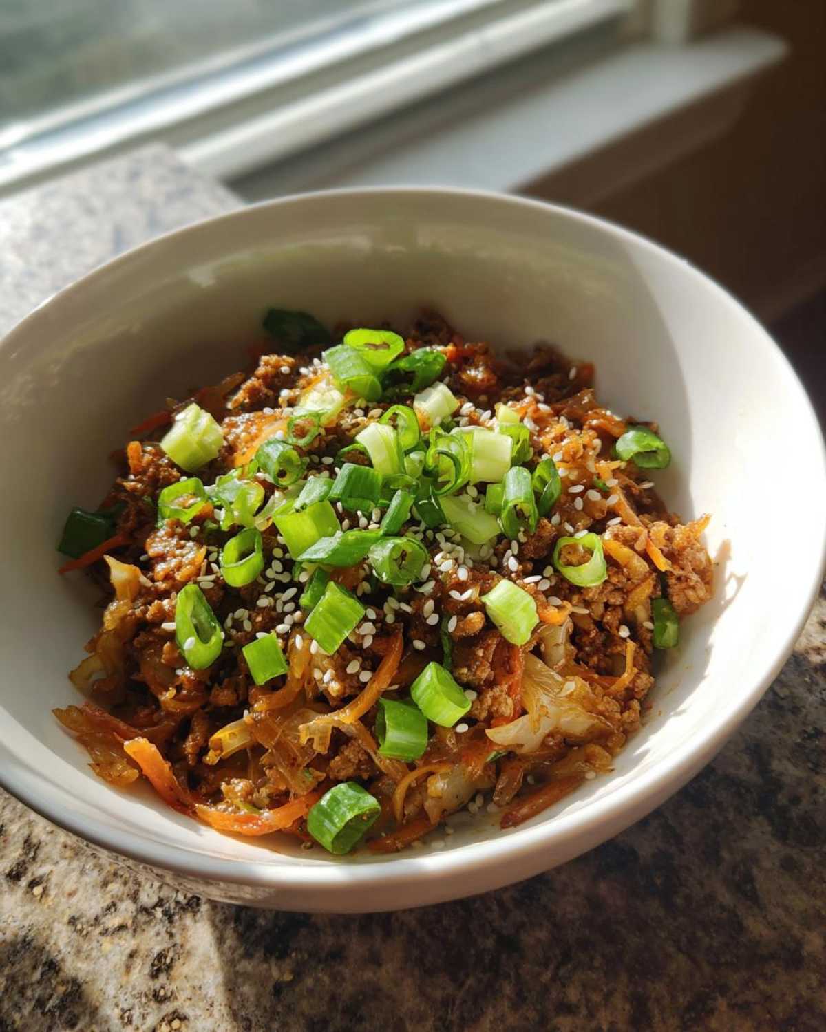 A close-up of a bowl of Egg Roll in a Bowl mixture topped with fresh green onions and sesame seeds.