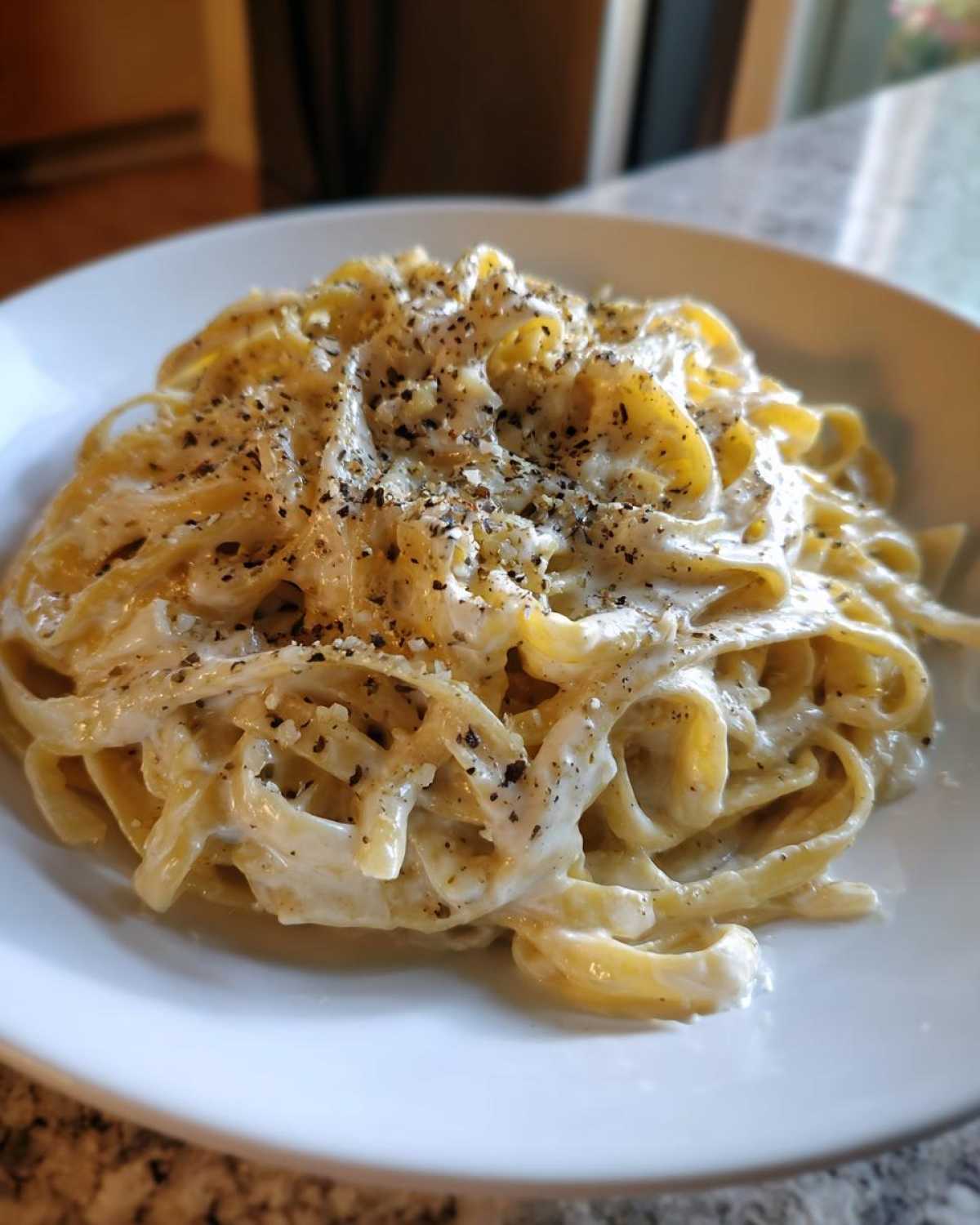 A close-up of fettuccine pasta generously coated in creamy homemade alfredo sauce and topped with cracked black pepper.