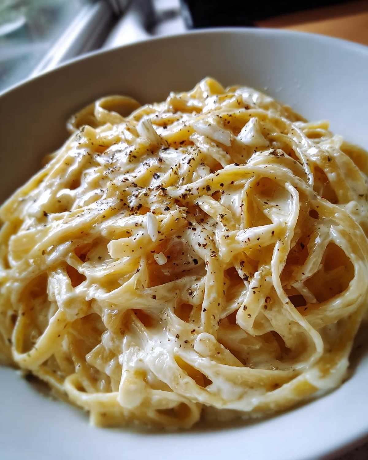 Close-up of fettuccine pasta coated in rich homemade alfredo sauce, topped with grated cheese and black pepper.