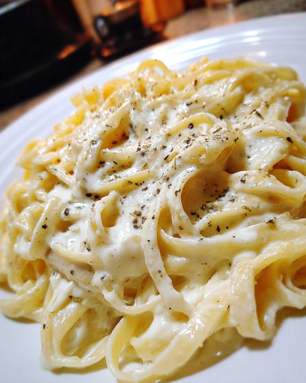 Close-up of fettuccine pasta coated in rich homemade alfredo sauce and sprinkled with black pepper and herbs.