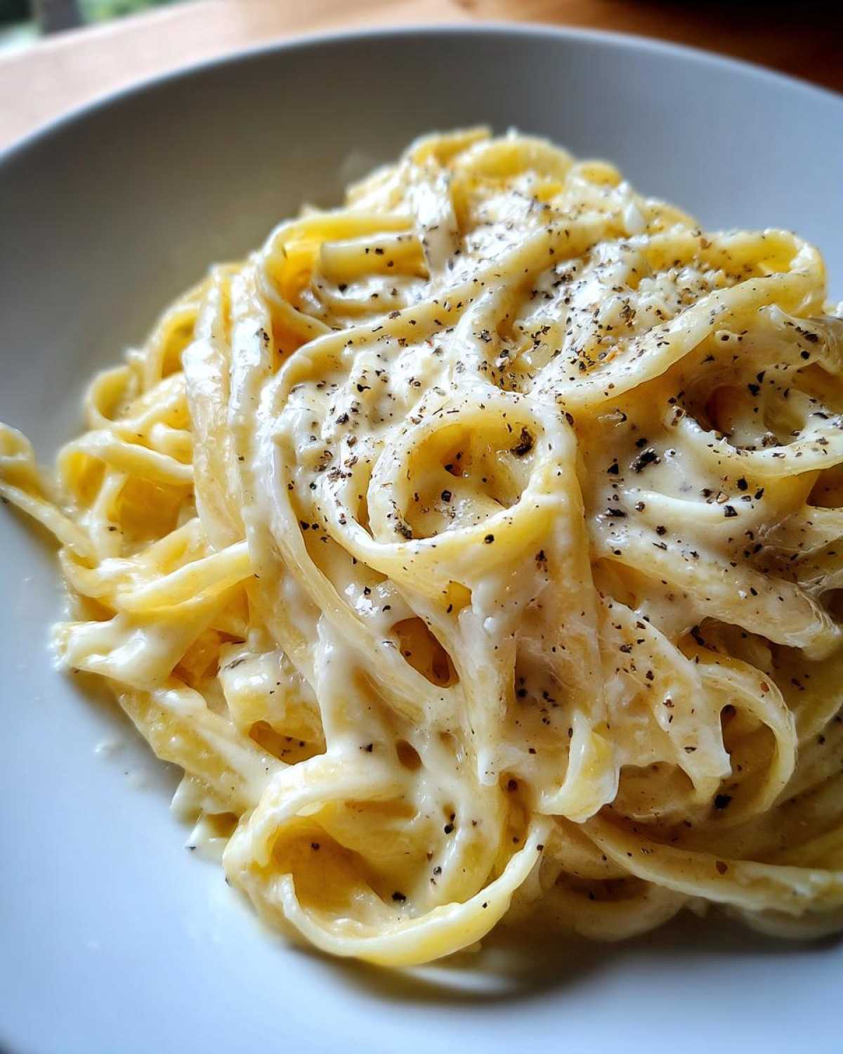 Close-up of fettuccine pasta generously coated in creamy homemade alfredo sauce and topped with cracked black pepper.