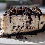Close-up of a thick slice of creamy oreo cheesecake topped with crushed cookies and chocolate sauce.