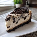 A perfect slice of creamy oreo cheesecake with chunks of cookie mixed in and topped with crumbs and a whole cookie.