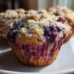 Close-up of a fluffy blueberry oatmeal muffin topped with coarse sugar, showing juicy berries bleeding into the sides.