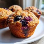 Close-up of a fluffy blueberry oatmeal muffin topped with coarse sugar, with more muffins blurred in the background.