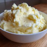 A close-up of creamy, fluffy Boursin mashed potatoes seasoned with black pepper, served in a white bowl.