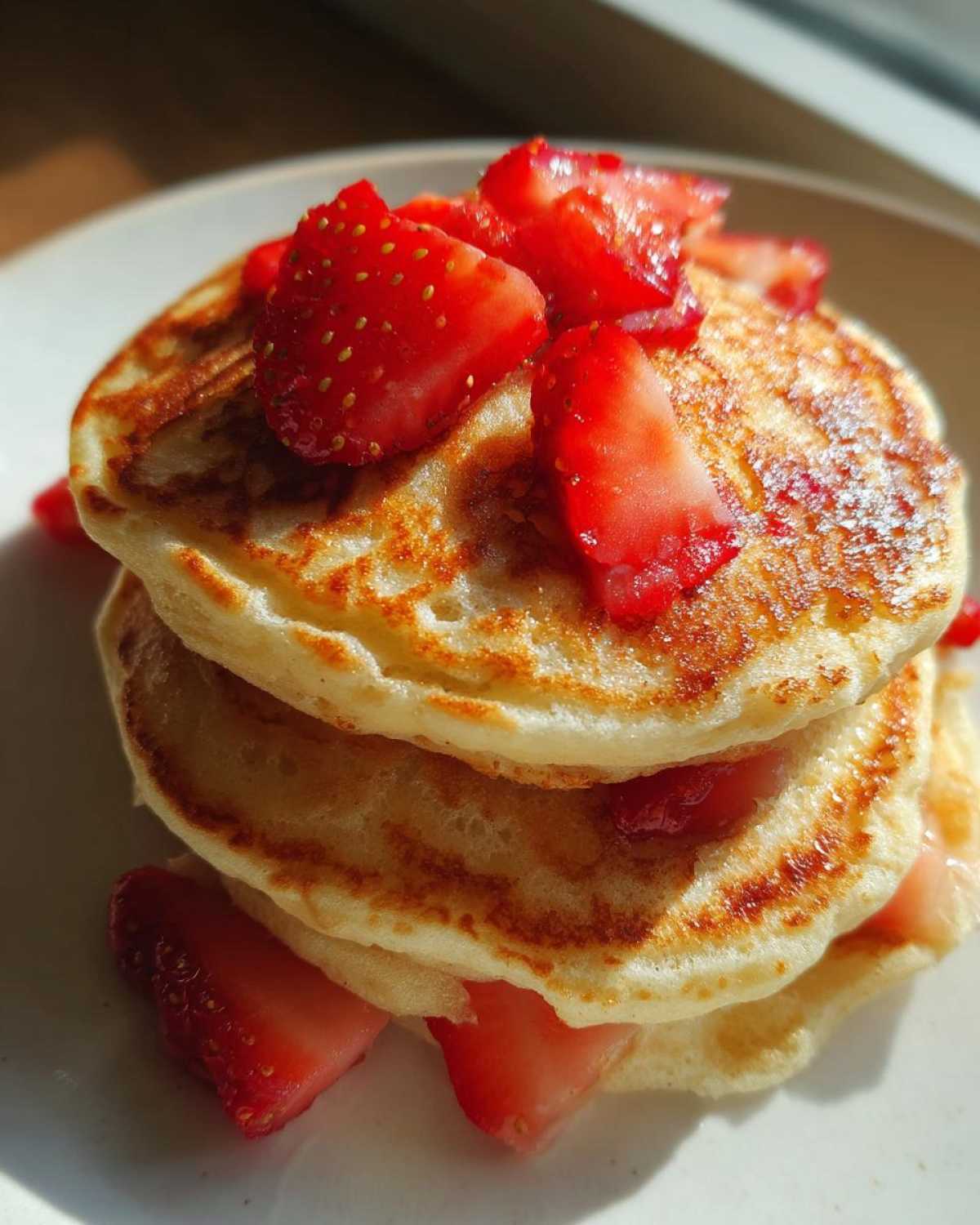 Close-up of a stack of three fluffy strawberry pancakes topped with fresh sliced strawberries.
