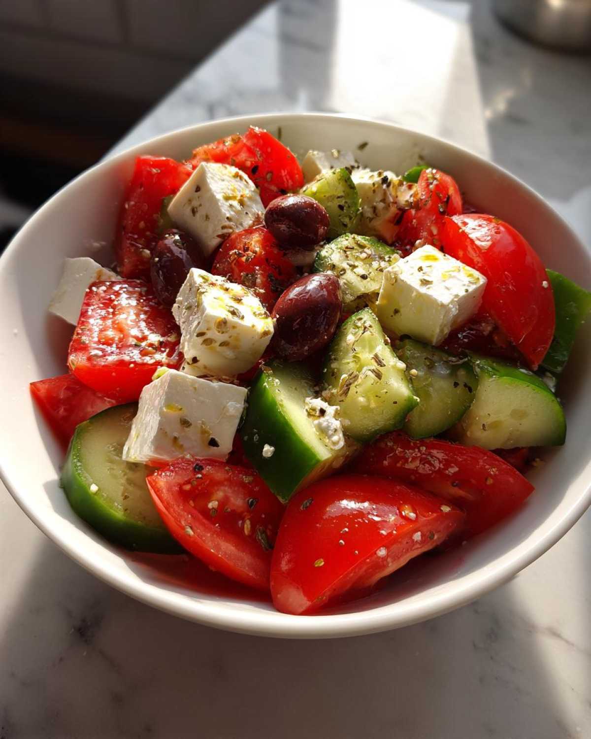 Close-up of a vibrant greek salad featuring chunks of tomato, cucumber, feta cheese, and Kalamata olives, seasoned with herbs.