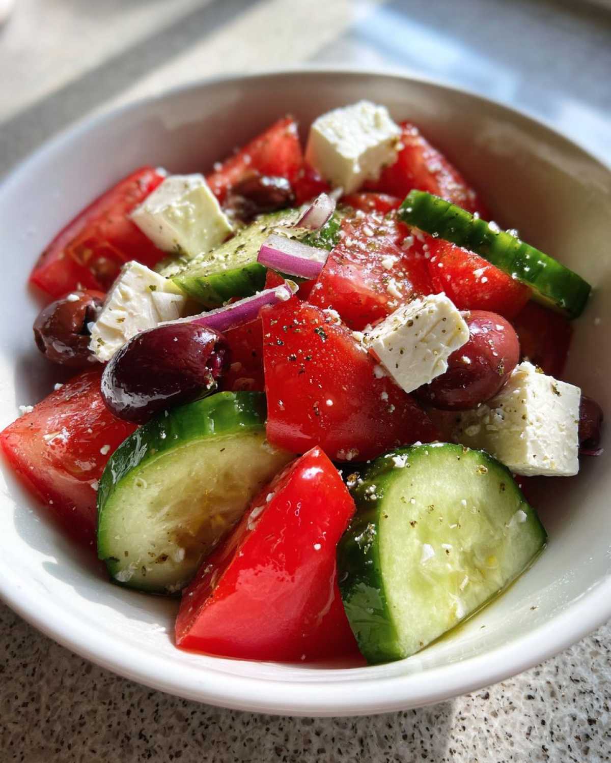 Close-up of a vibrant greek salad featuring chunks of tomato, cucumber, feta cheese, and Kalamata olives.