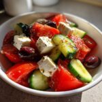 A close-up view of a vibrant greek salad featuring chunks of tomato, cucumber, feta cheese, and Kalamata olives.
