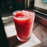 Close-up of a vibrant, icy strawberry daiquiri served in a tall glass on a marble surface.