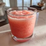 Close-up of a frosty, blended strawberry daiquiri served in a short glass on a white marble counter.