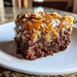 Close-up of a moist slice of german chocolate poke cake topped with gooey coconut-pecan frosting.
