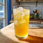 A tall glass filled with bubbly, yellow homemade lemonade and ice cubes, sitting on a wooden counter.