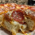 Close-up of a gooey pepperoni pizza sliders roll being pulled apart, showing melted cheese and seasoned bread.