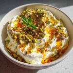 Close-up of a creamy ricotta dip topped with chopped pistachios, chili oil, and a mint garnish.