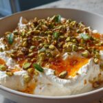 A bowl of creamy ricotta dip drizzled with spicy honey and topped generously with chopped pistachios and mint leaves.