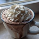 Close-up of a mug filled with rich homemade hot cocoa topped generously with whipped cream.