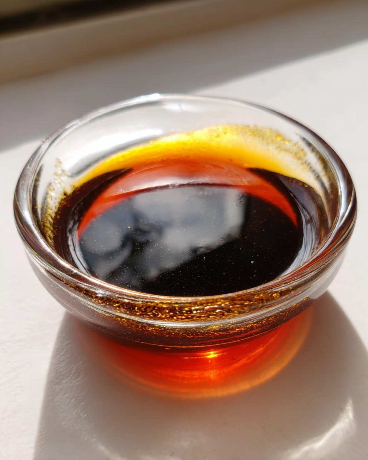 Close-up of dark, glistening homemade teriyaki sauce in a small glass bowl, catching the light.