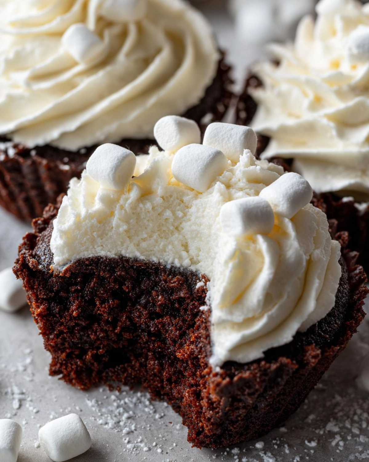 Close-up of a hot chocolate cupcake cut in half showing moist chocolate cake, white frosting, and mini marshmallows.