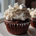 Close-up of a rich, dark chocolate hot chocolate cupcake topped with whipped cream and mini marshmallows.