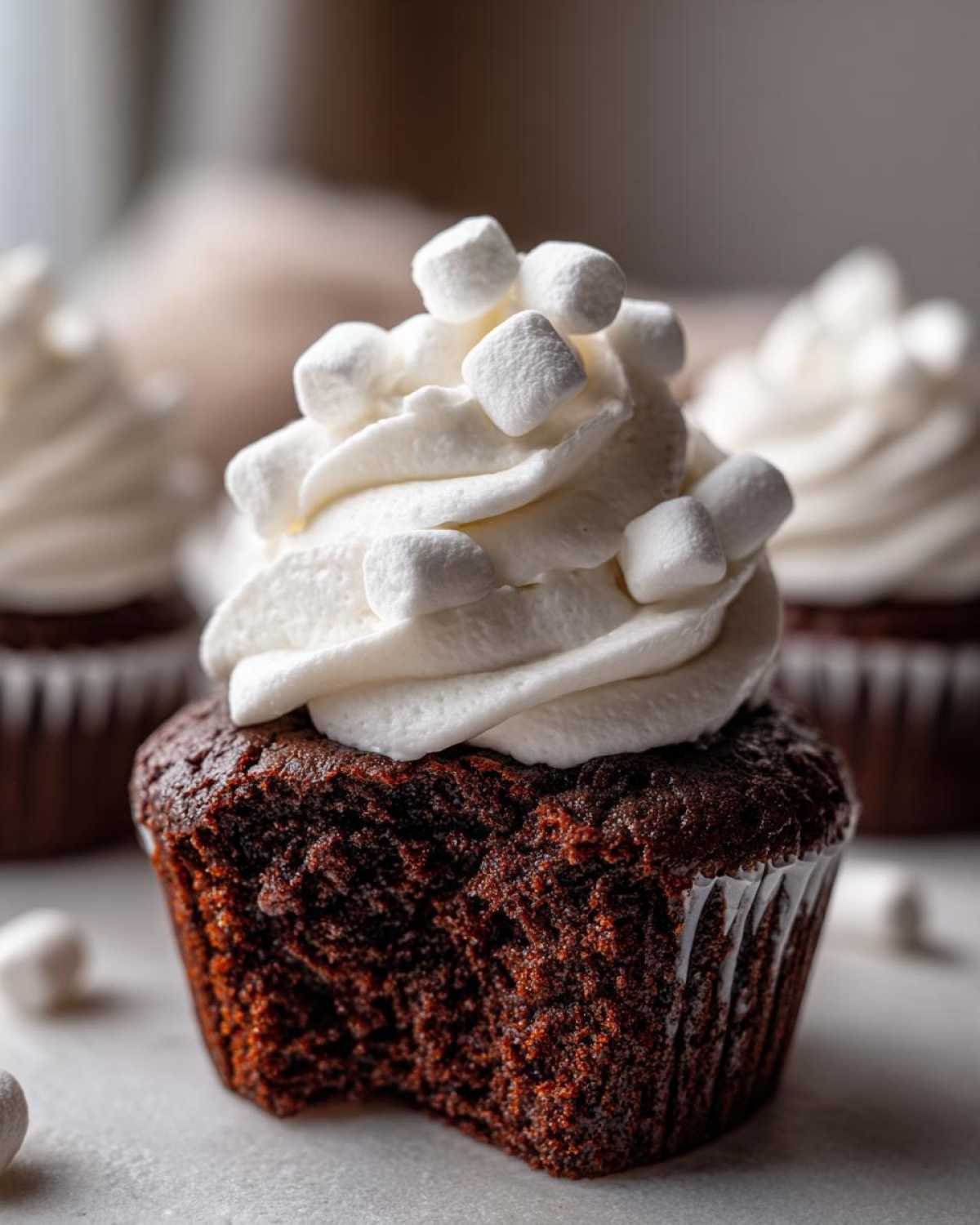 A close-up of a rich, dark chocolate hot chocolate cupcake with a swirl of white frosting topped with mini marshmallows.
