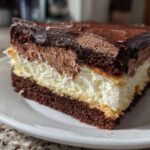 A rich slice of Italian love cake featuring three distinct layers: dark chocolate cake, white cream, and chocolate mousse, topped with ganache.