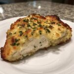 Cross-section of a juicy baked chicken breast topped with melted cheese and fresh parsley.