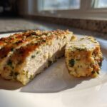 Close-up of a juicy baked chicken breast, sliced to show the moist interior and herb crust.