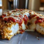 Close-up of a cross-section showing the juicy interior of a breaded chicken parmesan recipe topped with melted mozzarella and marinara sauce.