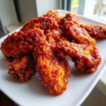 Close-up of crispy Korean fried chicken wings coated in a sticky, spicy red glaze served on a white plate.