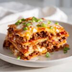 A layered slice of Mexican pizza featuring seasoned ground beef, melted cheese, and green onions.