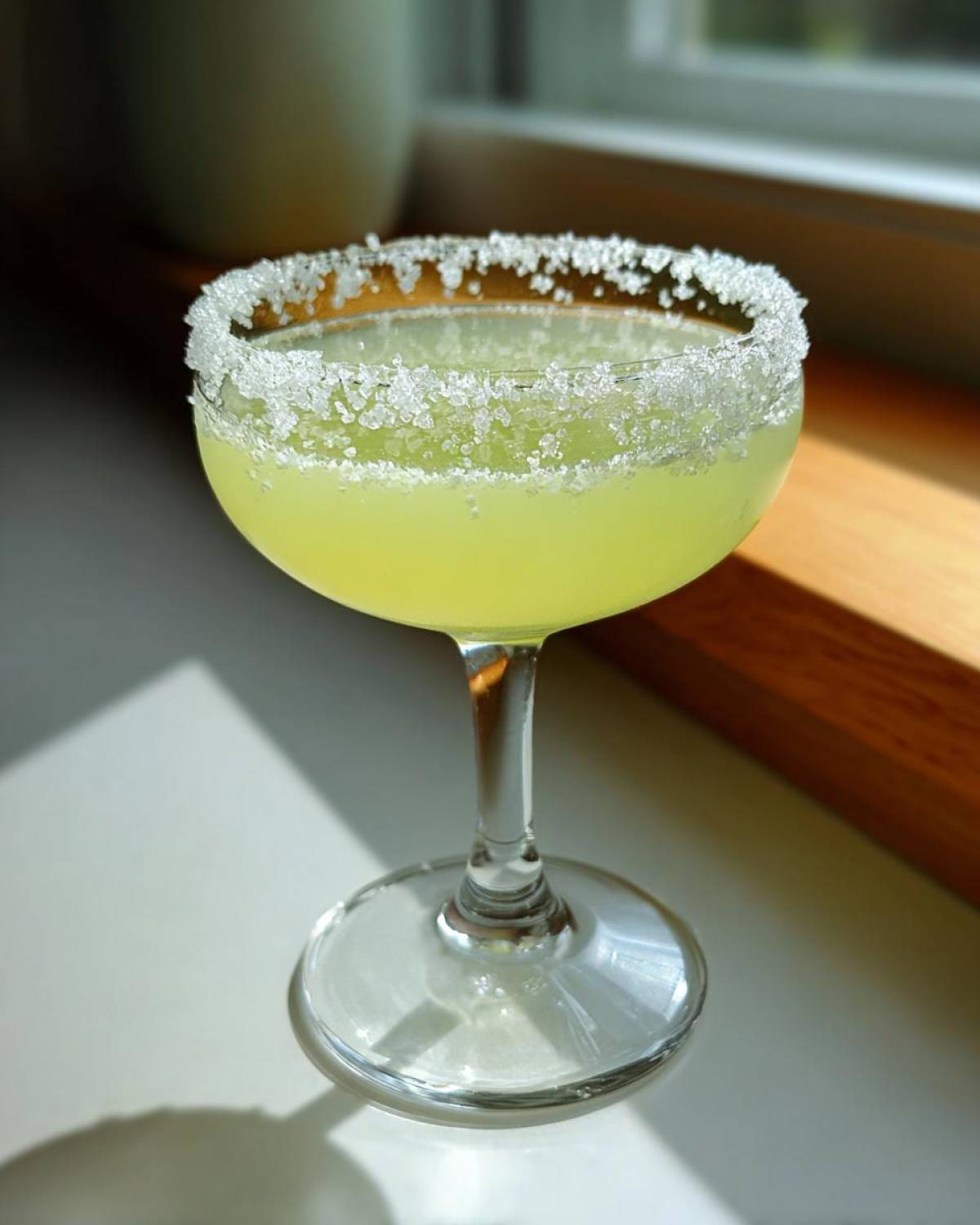A bright yellow lemon drop martini served in a coupe glass with a thick, glistening sugar rim.
