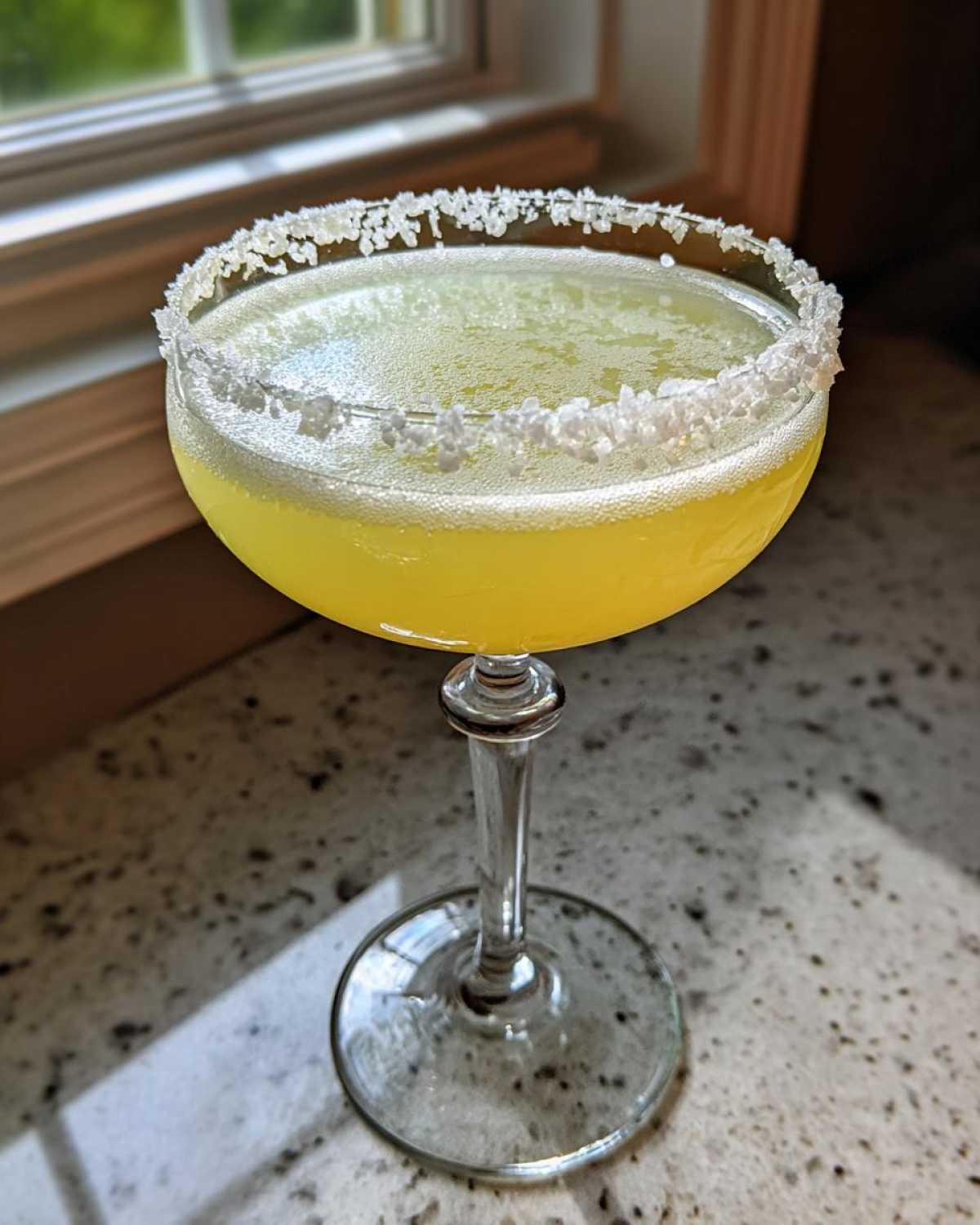 A bright yellow lemon drop martini served in a coupe glass with a thick, coarse sugar rim.