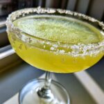 Close-up of a bright yellow lemon drop martini in a coupe glass with a thick, coarse sugar rim.