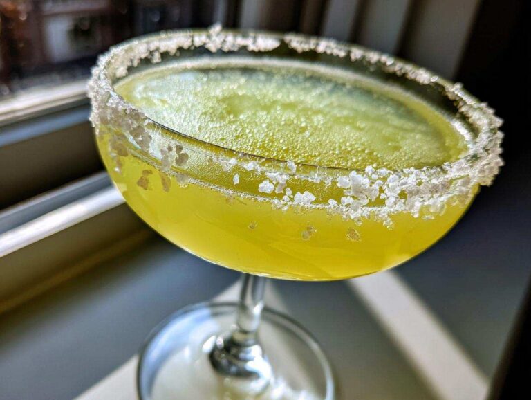 Close-up of a bright yellow lemon drop martini in a coupe glass with a thick, coarse sugar rim.
