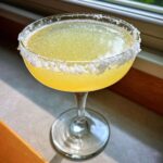 A bright yellow lemon drop martini served in a coupe glass with a thick, coarse sugar rim.