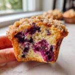 Close-up of a moist blueberry muffins half, showing the crumb texture and burst blueberries, topped with streusel.