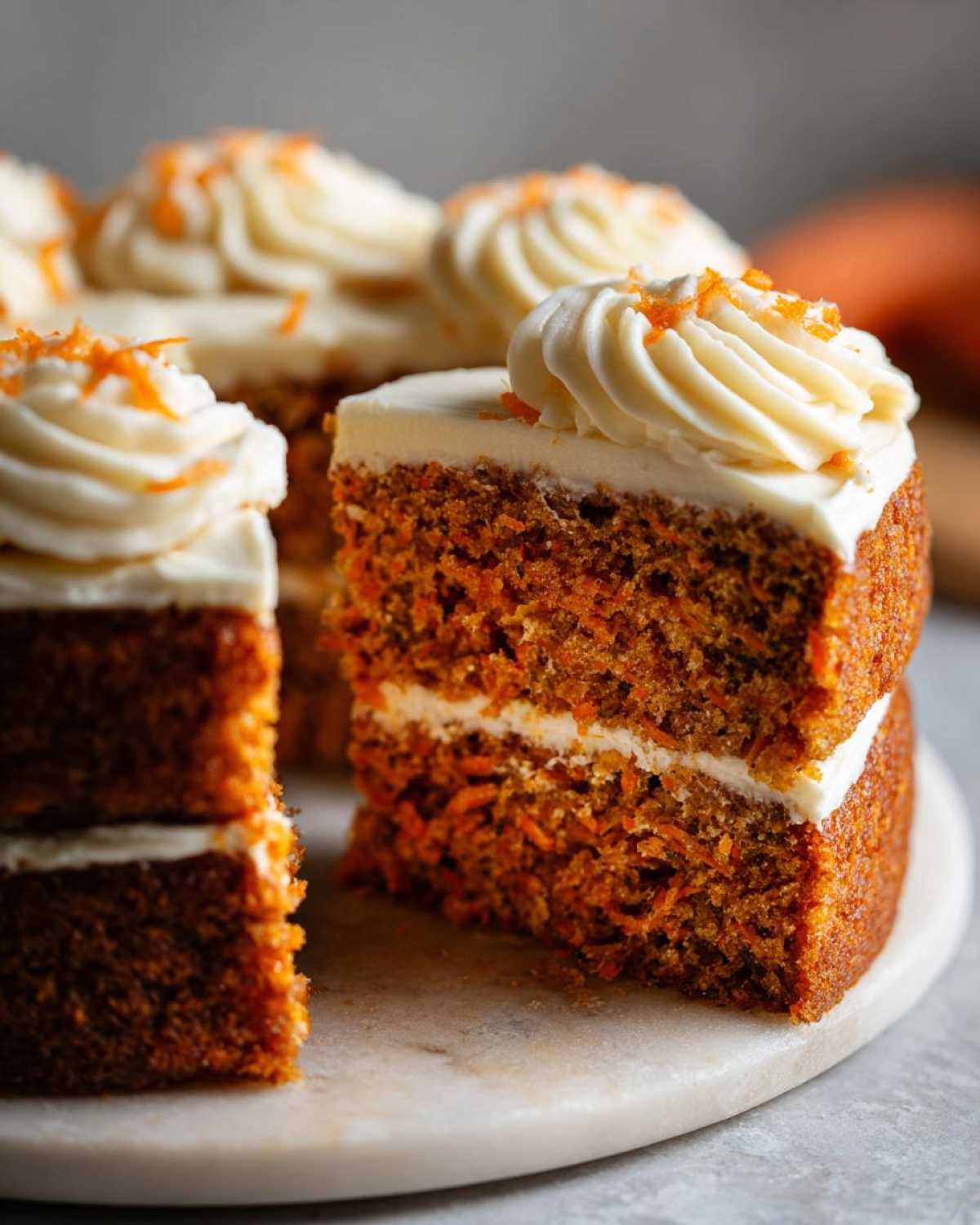 Close-up of moist slices of carrot cake recipe showing layers, cream cheese frosting, and shredded carrot topping.