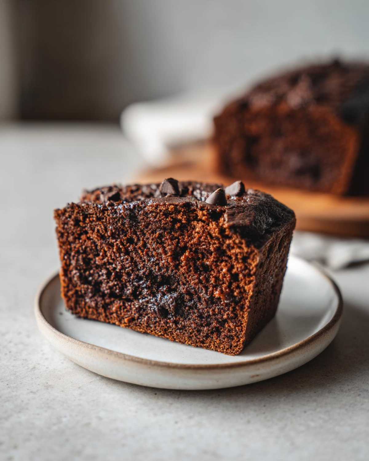 Close-up of a moist slice of chocolate bread topped with chocolate chips, served on a small plate.
