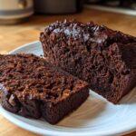 Two slices of rich, dark chocolate bread with a moist crumb and chocolate chips on a white plate.
