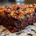 Close-up of a rich, moist slice of german chocolate poke cake topped with coconut pecan frosting.