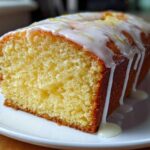 Close-up of a moist slice of lemon loaf cake topped with white glaze and lemon zest.
