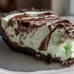 A close-up of a slice of no bake grasshopper pie showing the light green mint filling and dark chocolate crust with chocolate syrup drizzled on top.