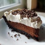 A perfect slice of no bake mud pie featuring a chocolate crust, rich chocolate filling, and whipped cream topping with chocolate shavings.