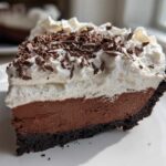A thick slice of no bake mud pie showing a dark chocolate crust, rich chocolate filling, and whipped cream topped with chocolate shavings.