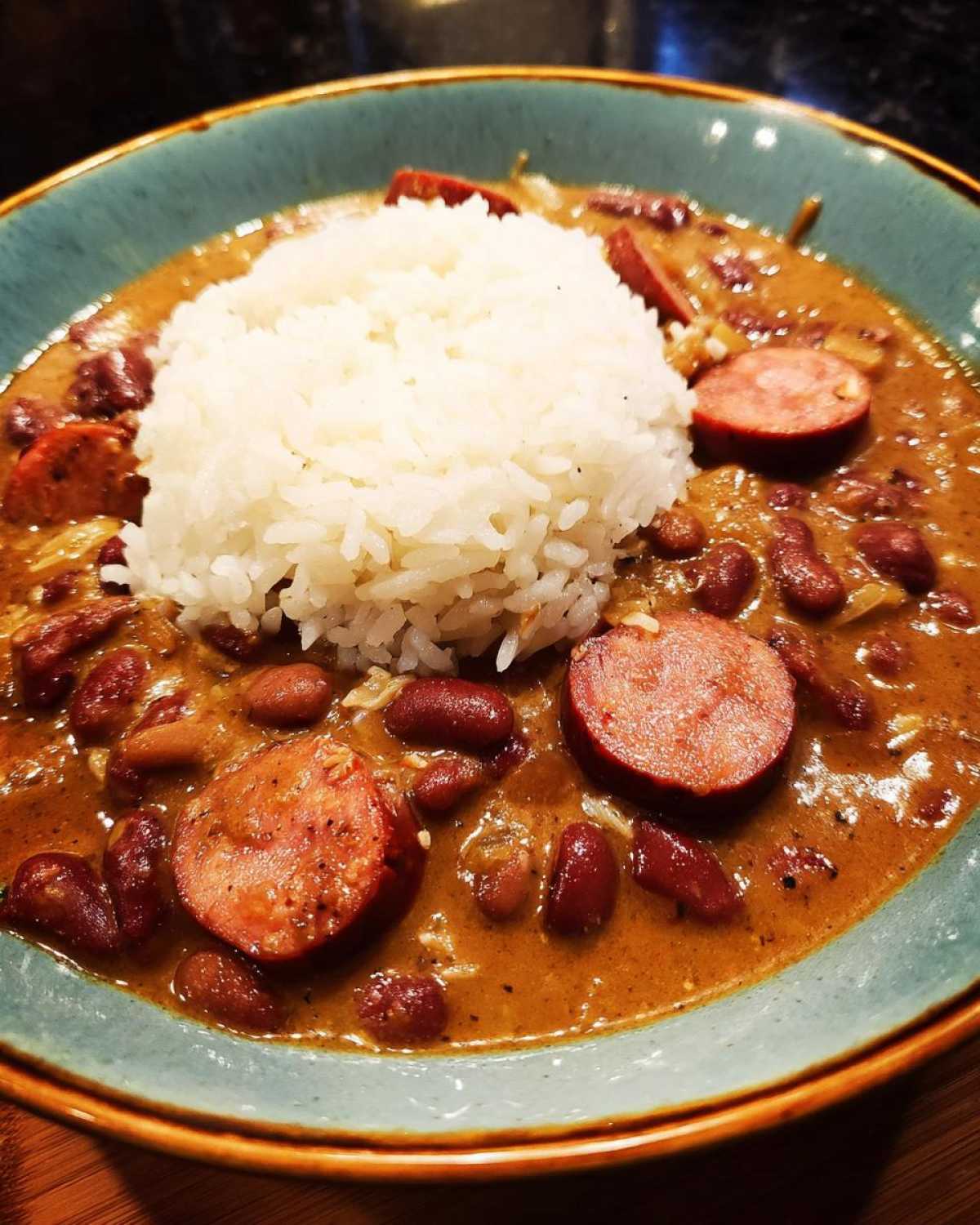 A close-up of a bowl of savory beans and rice topped with slices of smoked sausage.