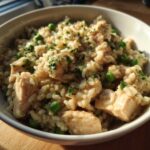 Close-up of creamy one pot chicken and rice with bright green peas and fresh parsley garnish.