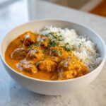 A white bowl filled with rich, orange pumpkin curry and a side of steamed white rice, garnished with fresh herbs.