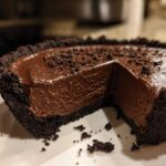 A decadent slice removed from a rich chocolate mousse pie with a dark chocolate crumb crust.